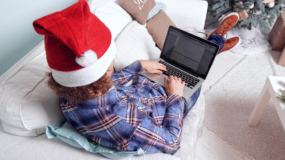 Man sitting on couch with santa hat and laptop